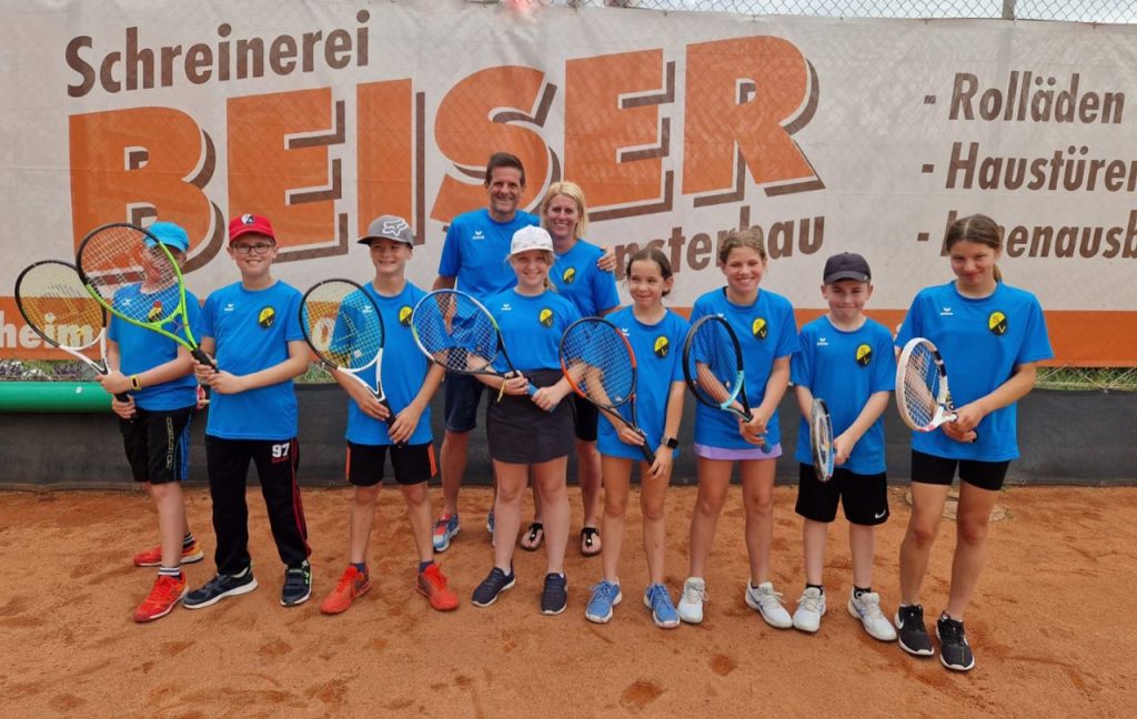 Bandenwerbung auf dem Tennisplatz Oberschopfheim. Davor stehen junge Tennisspieler*innen